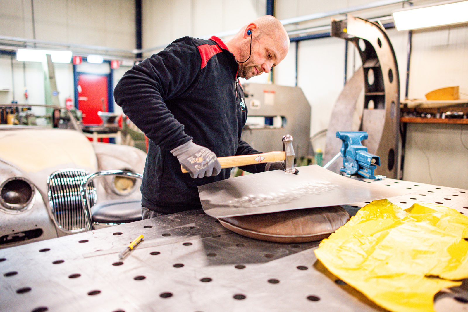Vakman vormt met de hand een aluminium carrosseriepaneel bij Vintage Coachworks